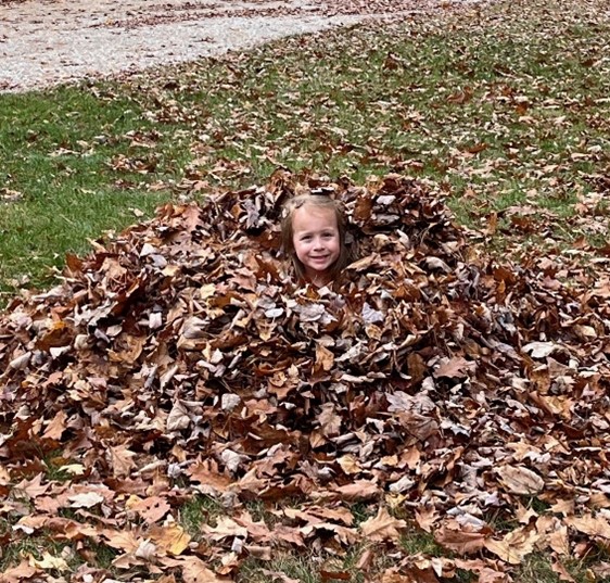 A girl hiding in a pile of leaves.